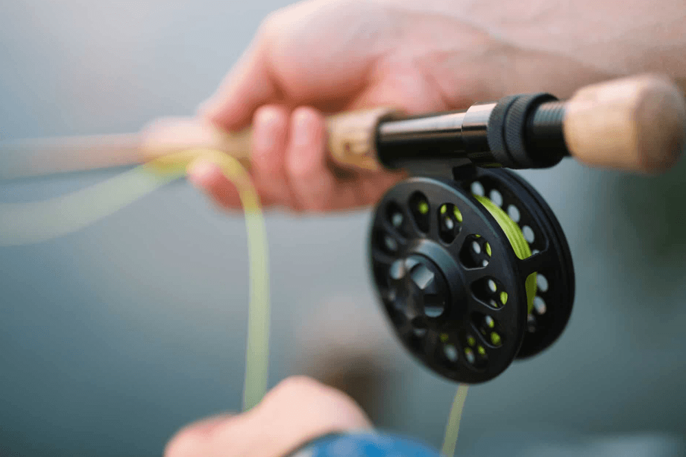 A close-up of a hand gripping a fishing rod and reel with green fishing line.