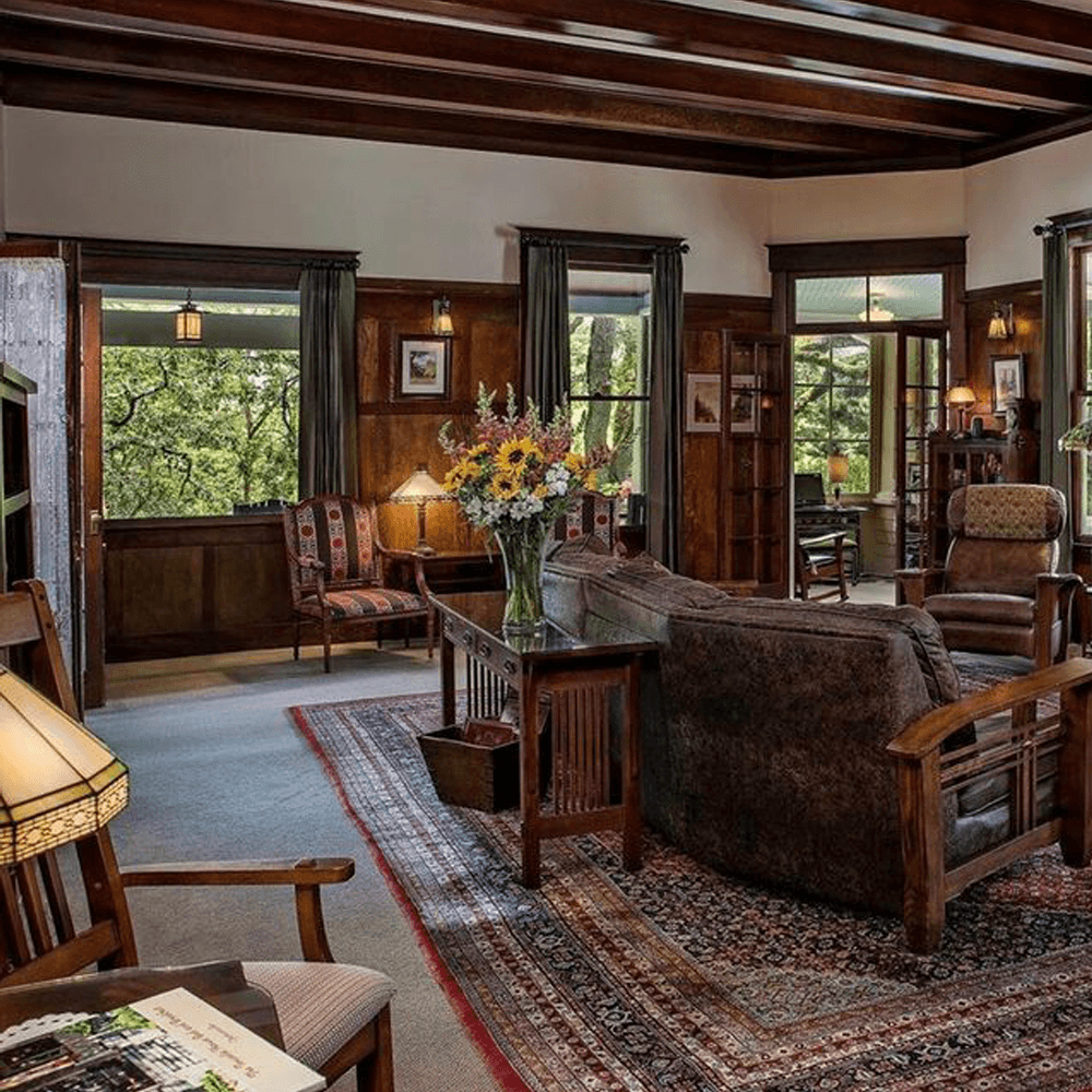 Cozy living room with wooden accents, floral arrangements, and large windows.